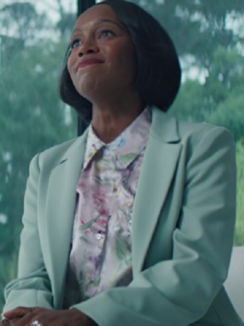 Aja Naomi King in a mint green blazer, sitting comfortably on a couch, portraying her character in Grosse Pointe Garden Society.