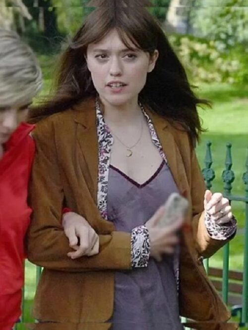 Aimee Lou Wood, in Toxic Town (2025), is seen sitting on a park bench wearing a stylish Toxic Town 2025 Aimee Lou Wood Brown Blazer with button details and a floral-patterned inner lining. She pairs it with a dark lace-trimmed camisole and blue jeans. With a serious expression, she gazes to the side while holding a beverage can. The background features a grassy park setting with a soft blur.