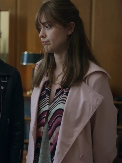 Aimee Lou Wood is seen wearing the Toxic Town Aimee Lou Wood Pink Coat, which is a stylish and elegant trench coat in a pastel pink color. The coat's soft hue and tailored fit add a sophisticated touch to her outfit, which also includes a patterned blouse and dark pants. This look is set in a classic office environment, and it combines vintage charm with contemporary fashion.
